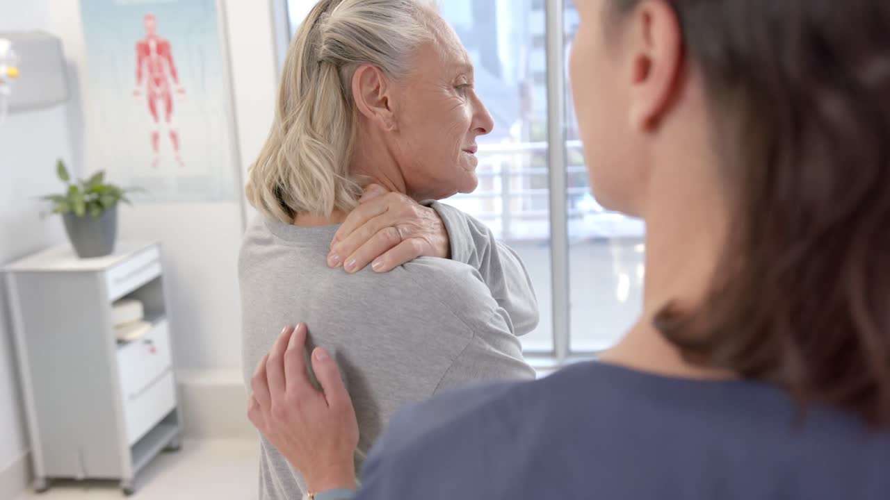 Caucasian female physiotherapist massaging back of female senior patient at rehab center