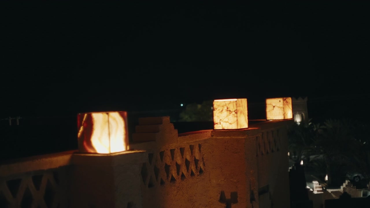 Lanterne di Pietra Illuminate che Fiancheggiano un Muro Ornato di Kasbah di Notte in un'Oasi Marocchina