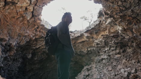 young man looks around in awe at massive cave with hole in roof, slow motion