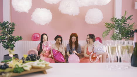 front view of four  women with headdresses throwing ballons sitting on the sofa