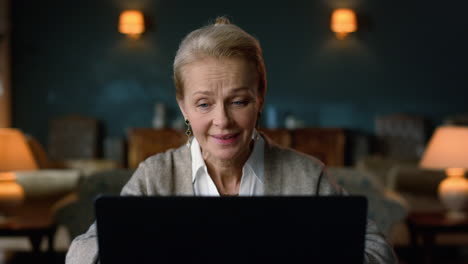 old aged woman having video call on laptop computer in classic interior