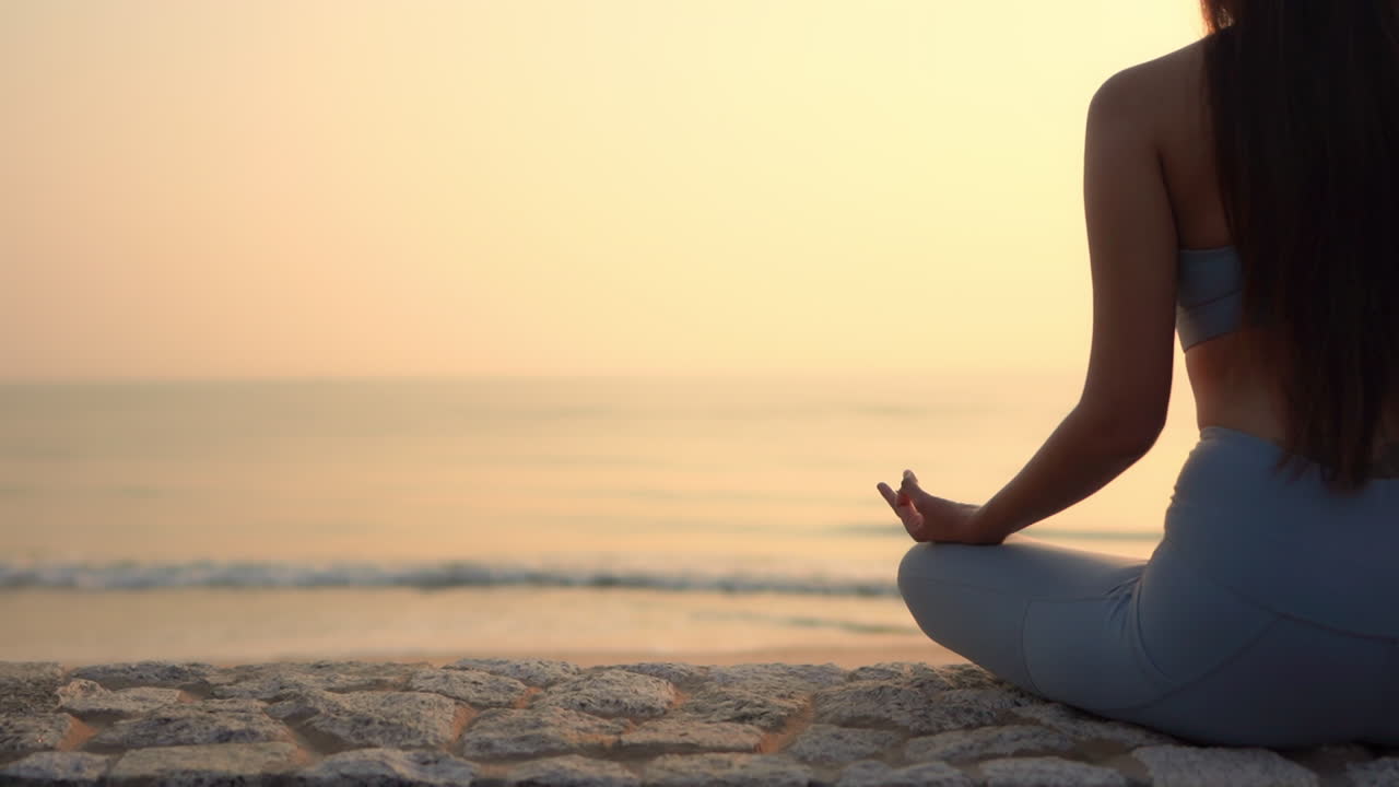 Rule of thirds close-up woman sitting in the Sukhasana pose on the beach at sunset. Copy space