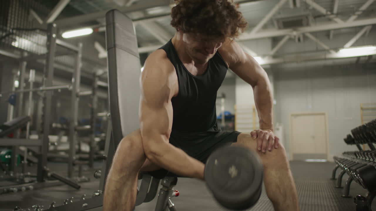 Strong Man Performing Dumbbell Bicep Curls in Modern Gym