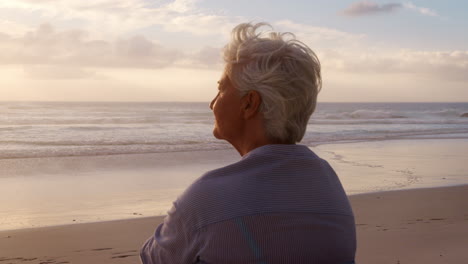 rear view of senior woman on beach watching sun set over ocean