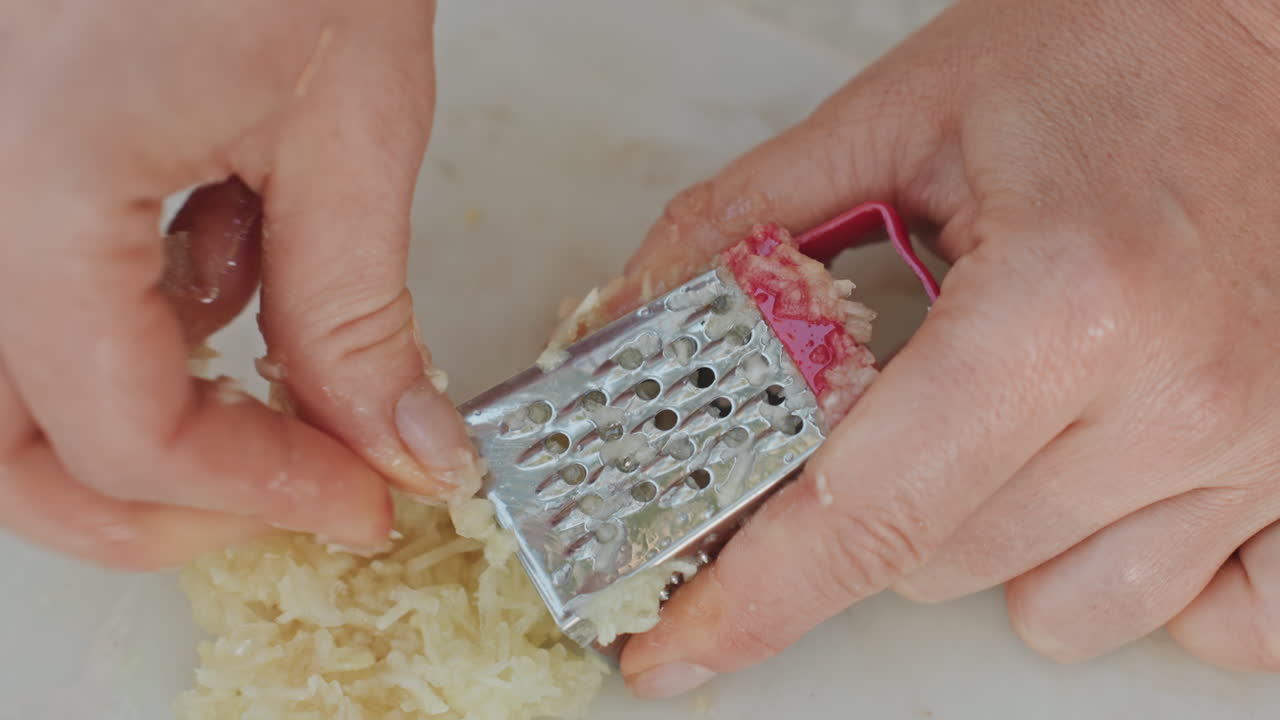 Una camperista grattugia abilmente l'aglio su un tagliere, una grattugia compatta crea scaglie delicate, ritmo paziente e mani ferme, atmosfera da cucina rustica all'aperto, preparazione degli aromi per uno stufato da campeggio.