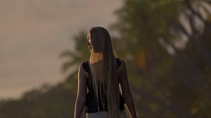 Un momento sereno mentre una donna cammina a piedi nudi lungo le rive dorate della spiaggia di Uvita al tramonto, con la luce calda che proietta lunghi riflessi sulla sabbia bagnata e la giungla sullo sfondo.