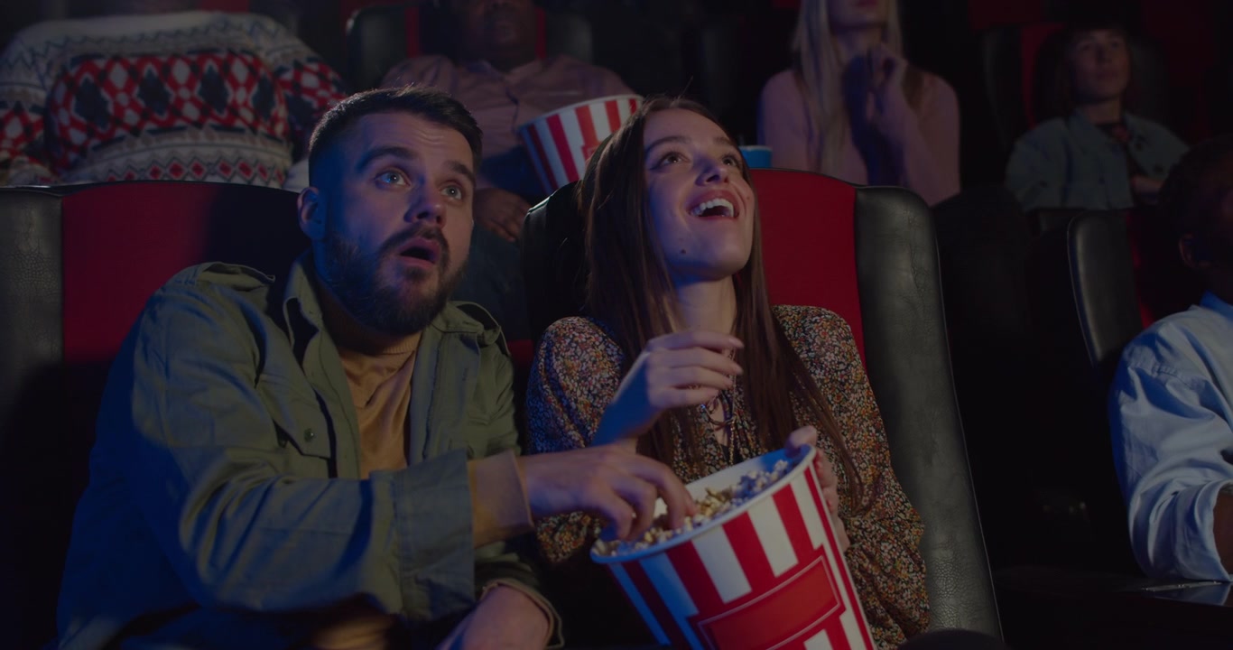 Giovane coppia che mangia popcorn e guarda un film al cinema