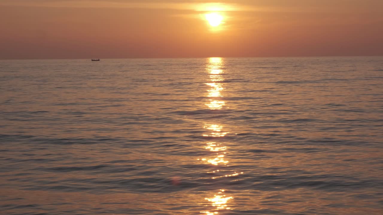ocean at sunset with golden light and small fishing boat in distance
