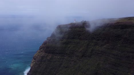 Madeira-Island,-Portugal---Lighthouse-Tower-Fringed-On-Top-Of-A-Cliff-Covered-By-Moving-Clouds,-Overlooking-The-Calm-Ocean---Aerial-Drone-Shot