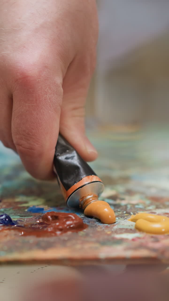 el creador aplasta la pintura de un tubo de metal en el escritorio de primer plano. el artista hábil exprime el pigmento acrílico naranja para obras de arte en la tienda. suministros del pintor