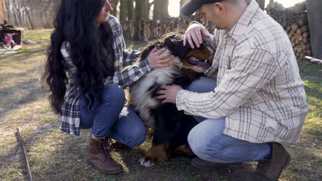 Close-up-view-of-caucasian-couple-squatitng-and-petting-their-dog-in-the-countryside