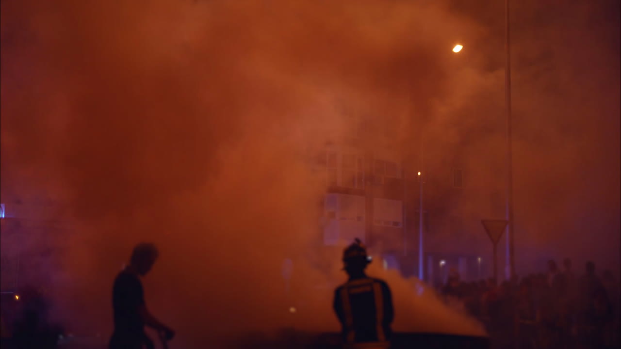 People Silhouetted in Dense Smoke on a Night Street