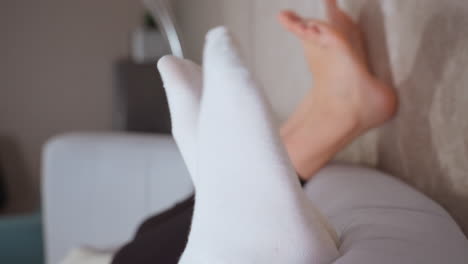close up leg view of people playfully moving legs while lying on couch in cozy setting, focus on white socks and bare feet in motion against neutral background