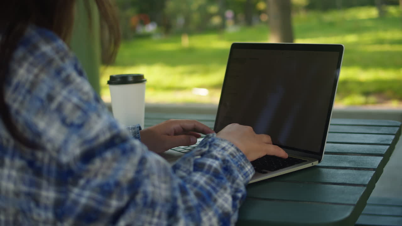 Woman is working with laptop in the green park co-working. Chatting with netbook outdoor close-up.
