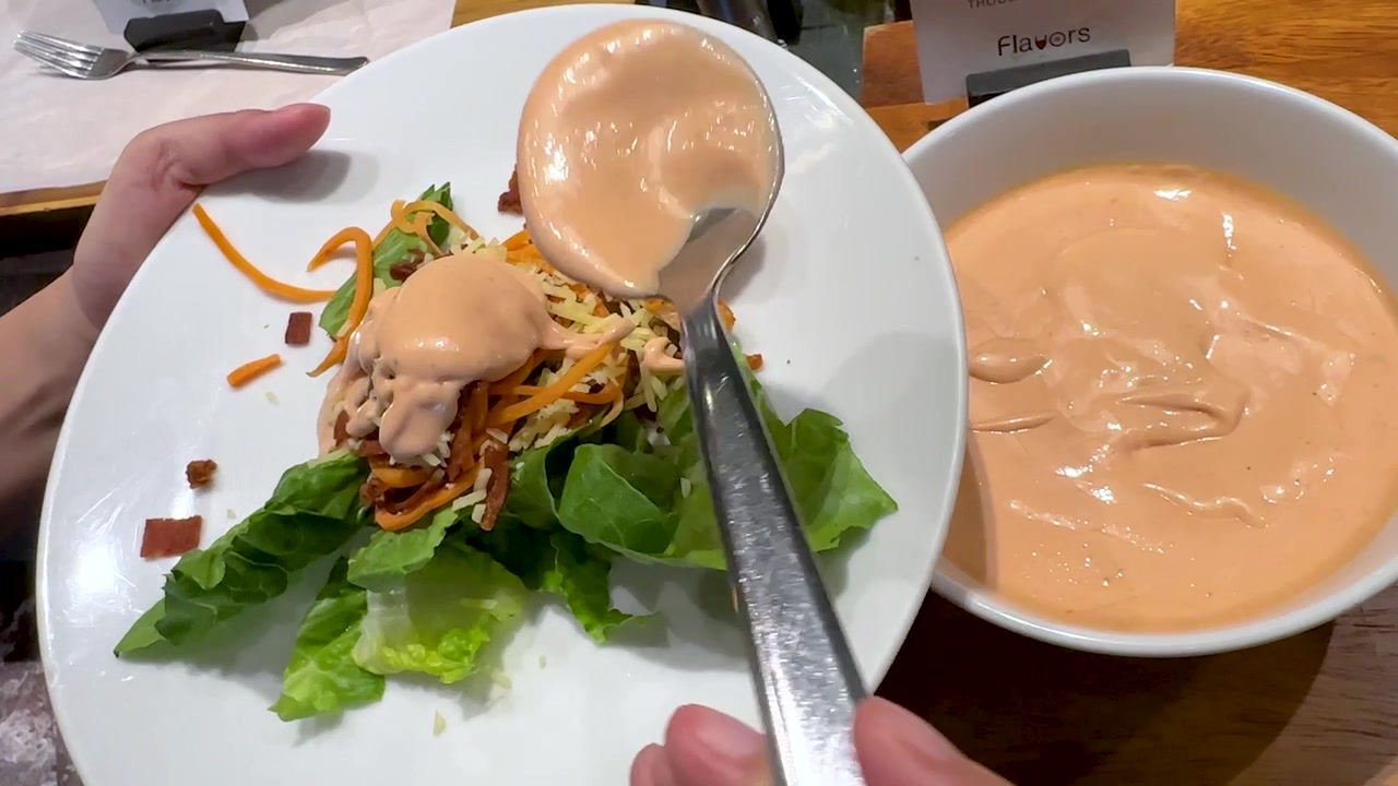 A metal spoon pours orange dressing onto a salad plate with lettuce and croutons