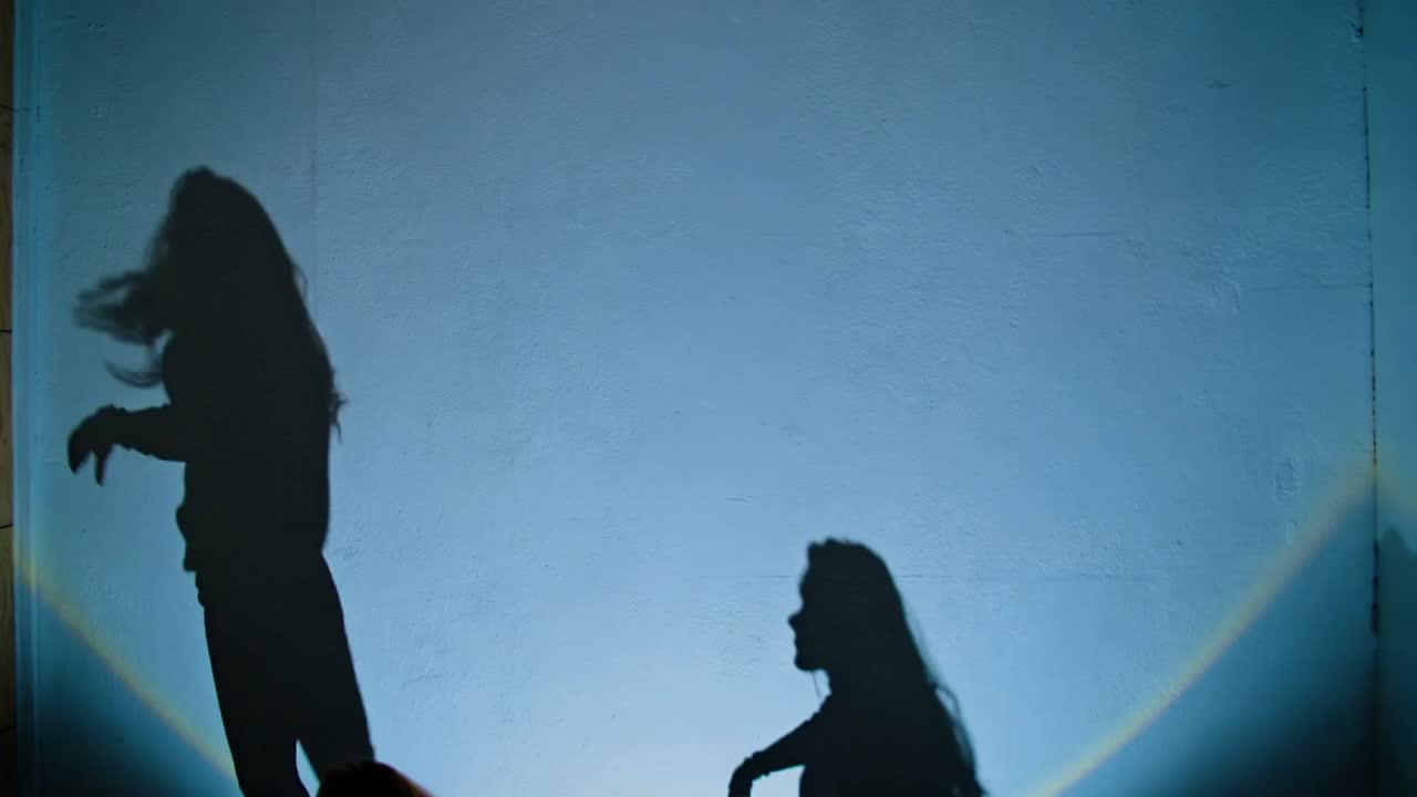 Moving group of dancers wearing dark clothing, reaching on screen, backlight cueing dance