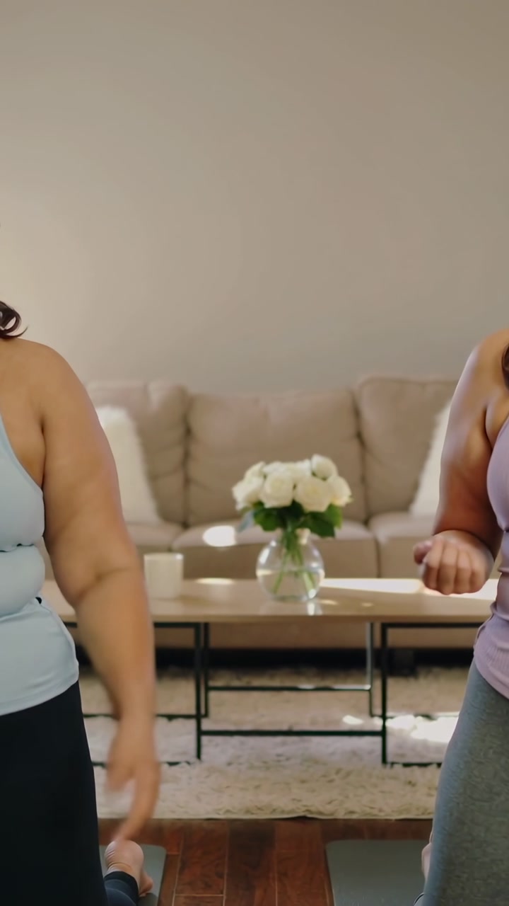 Vertical video: Two women kneeling on mats following cue lowering rotating arms for fitness at home
