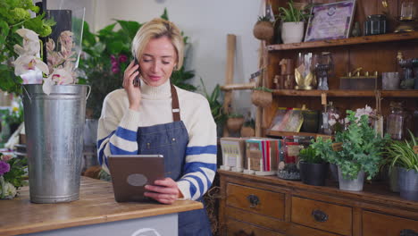 female owner of florists shop with digital tablet talking on mobile phone