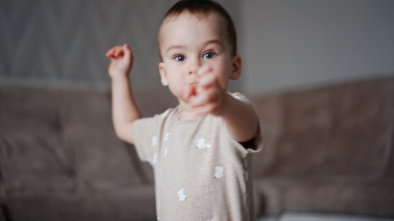 Small baby boy runs into the room. Kid notices the camera and stretches hands to it.