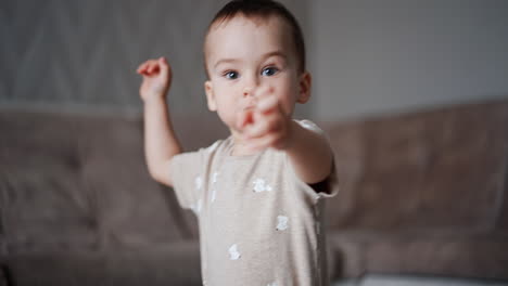small baby boy runs into the room. kid notices the camera and stretches hands to it.