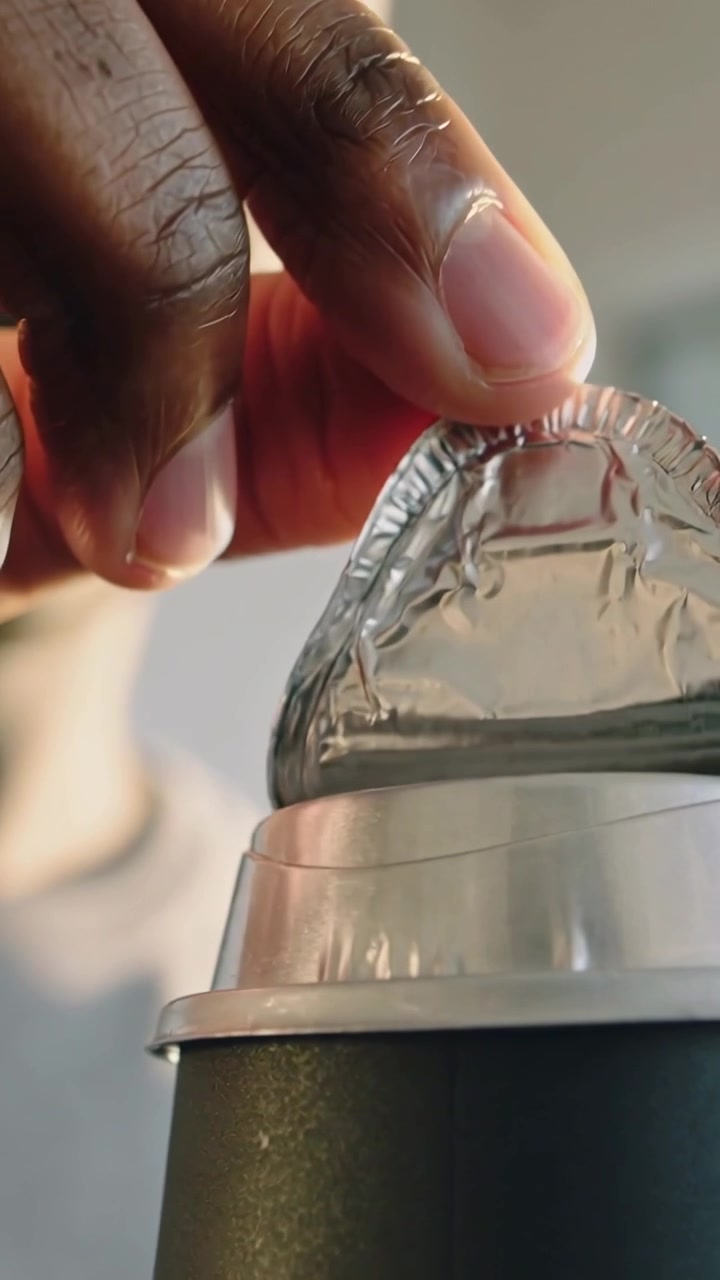 Video verticale: Polpastrelli che iniziano a sollevare la pellicola da una capsula di caffè in cucina, mentre si prepara il caffè.