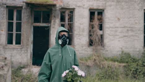 survivor holding flowers on ruined building background. person in chemical safety suit and respirator standing with flowers in hands in abandoned place. chemical attack.
