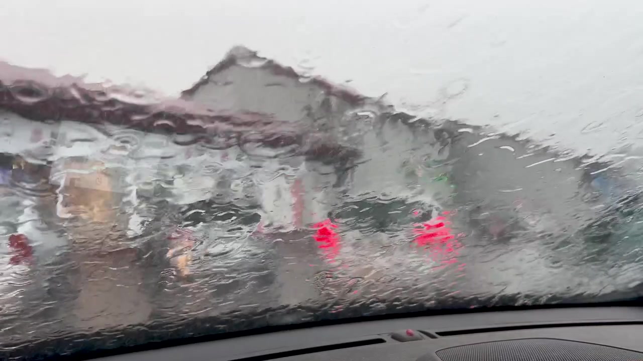 Dramatic view of intense rainfall washing over a vehicle windshield with blurry traffic lights in the background. Cinematic depiction of bad weather and road safety.