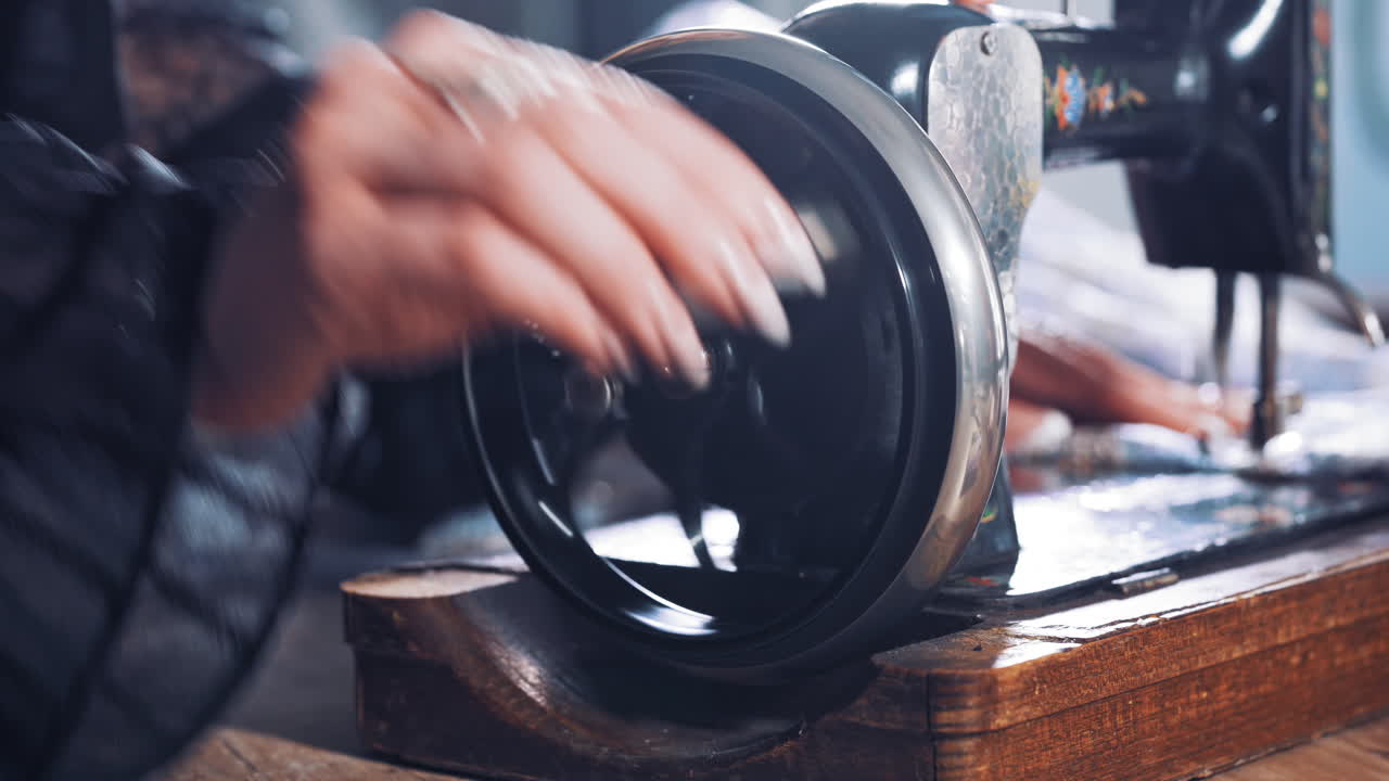 Close-up of woman's hand spinning the metal wheel of an old sewing machine. Seamstress is working on a black sewing machine in atelier. Craft and handmade concept.