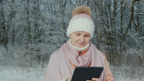 Una-Mujer-Con-Una-Chaqueta-Rosa-Disfruta-De-Un-Paseo-En-Un-Parque-De-Invierno-Utiliza-Una-Tableta-Digital