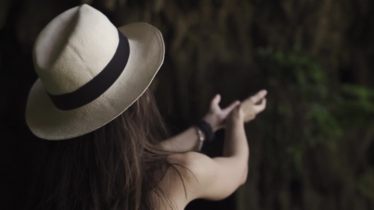 Young women's with fashionable hat exploring a cave and catching dripping water from its rocks