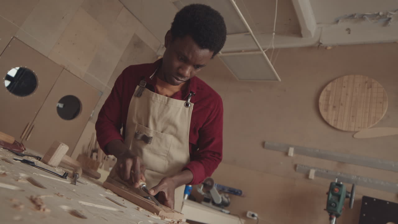 African American Joiner Carving Wooden Board in Workshop