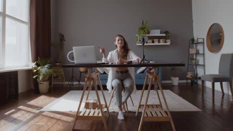 campo lungo di una giovane donna vlogger che fa un live streaming con due fotocamere, laptop e smartphone