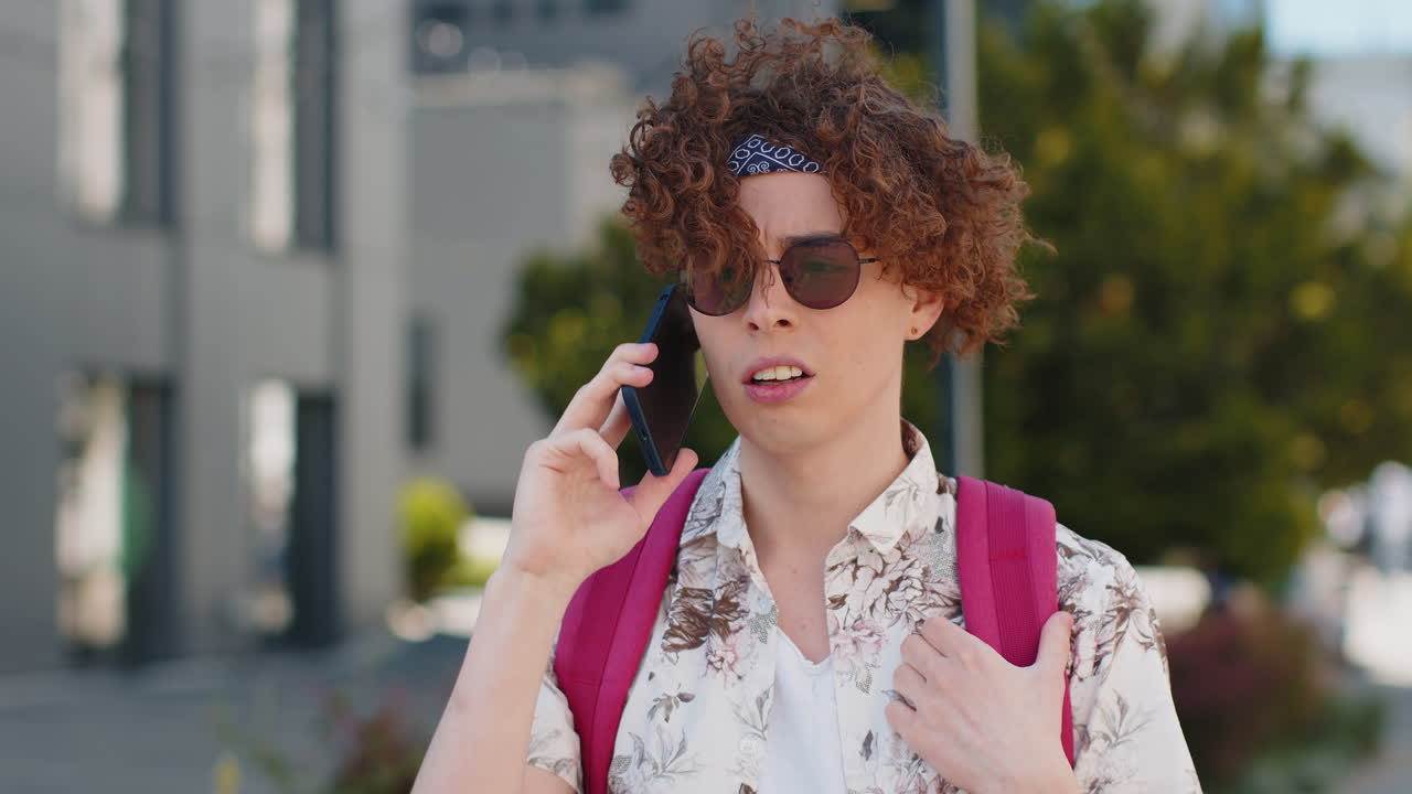 joven con gafas de sol y camisa floral posando en una calle de la ciudad