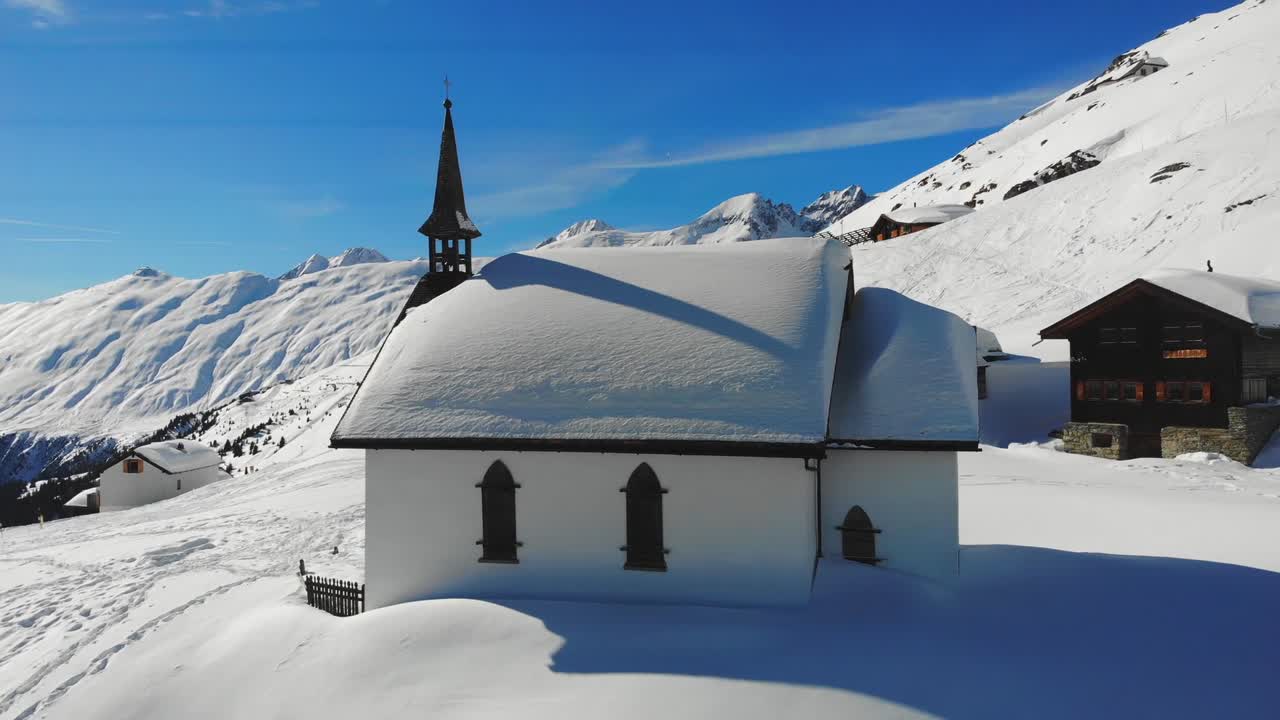 Drone captures breathtaking view of snowcapped building nestled in picturesque landscape, surrounded by Switzerland's stunning scenery, illuminated by bright daylight and blue sky