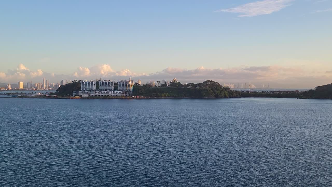 A beautiful aerial view captures the modern Panama City skyline and coastal islands bathed in the warm, golden light of a spectacular sunrise or sunset over the Pacific Ocean.