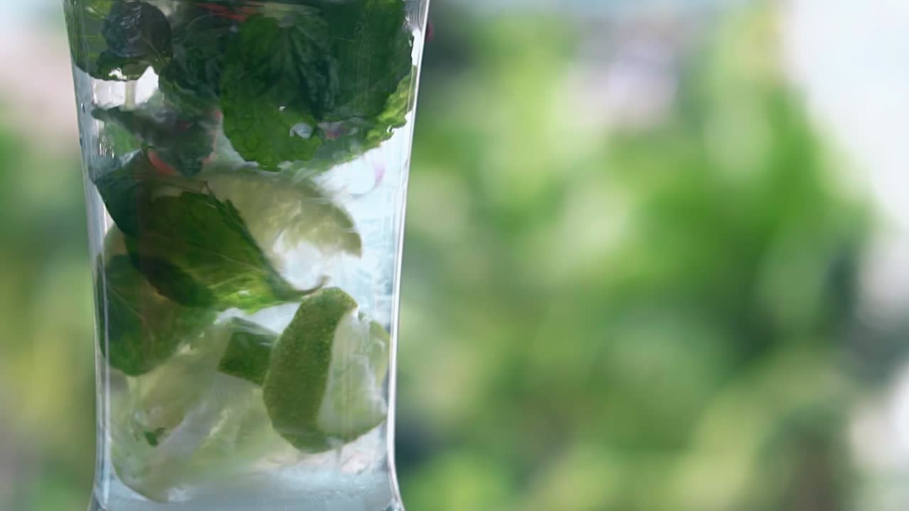 la paja de plástico roja se mueve lentamente en el vidrio brillante con mojito