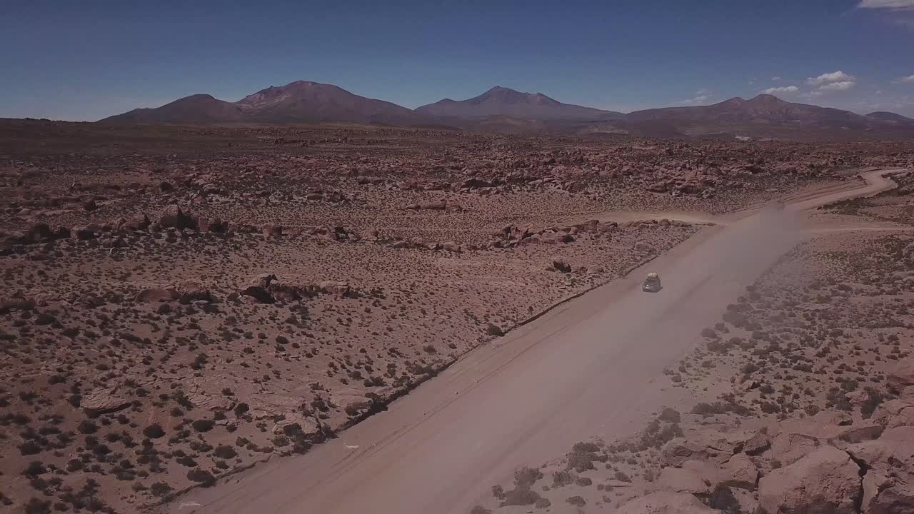 Aerial view of a 4x4 on a dusty red road at the Eduardo Avaroa National Andean Wildlife Reserve, slowly lifting the view to open up to the valley of rocks, "Valle de Rocas" in Uyuni, Bolivia