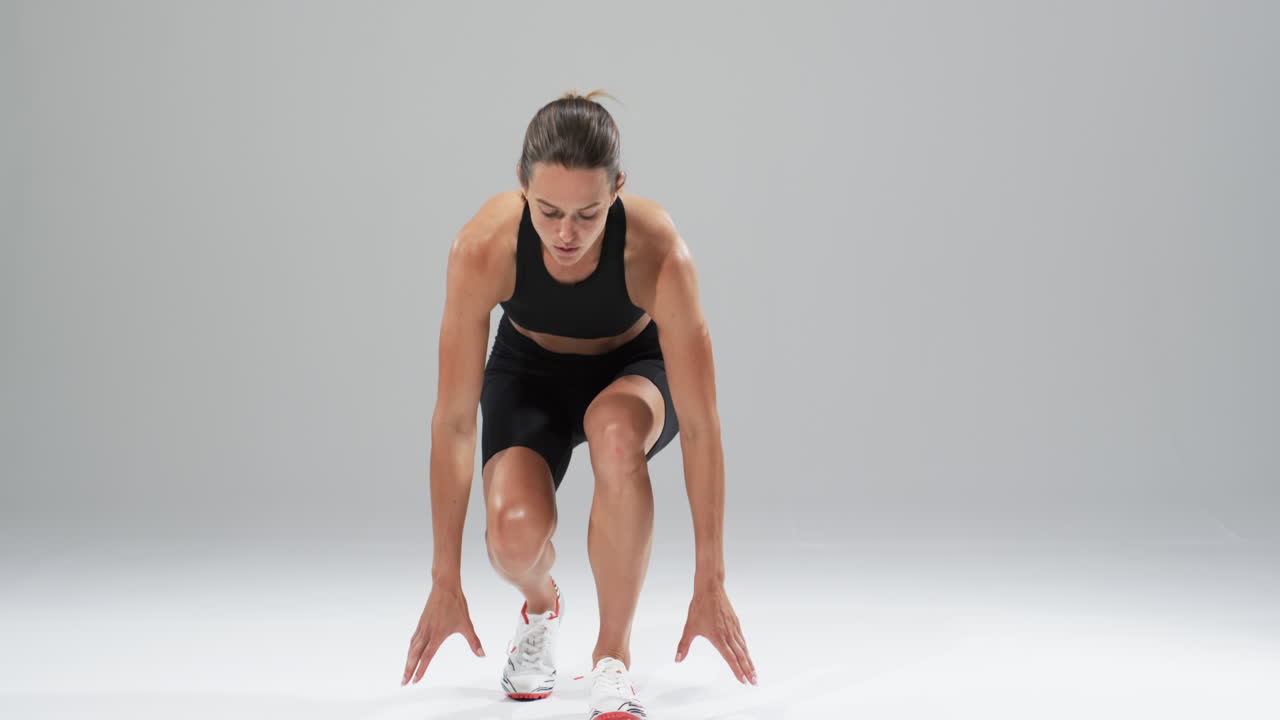 Young Caucasian woman athlete in athletic wear prepares to run on a white background, with copy spac