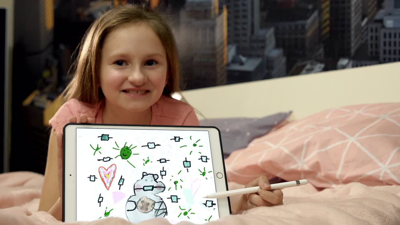 소녀는 의료 마스크에 고양이를 그렸고 카메라에 그녀의 그림을 보여줍니다.