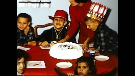group of children sitting around a cake on a table. circa usa - 1970s: a group of children sitting around a table, enjoying a cake in a 1970s video from the usa.