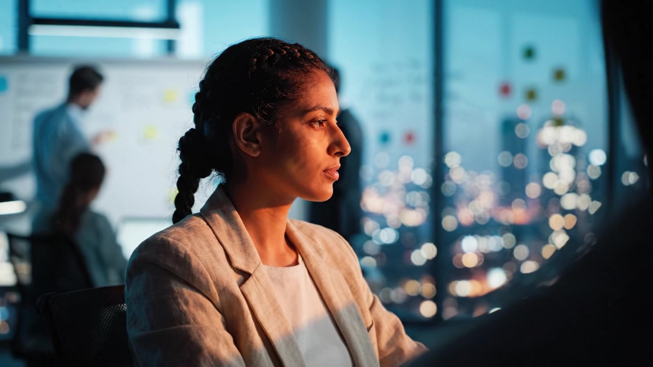Focused Professional Woman in Modern Office Environment, Engaged in Work and Surrounded by Team Members, Capturing the Essence of Collaboration and Leadership