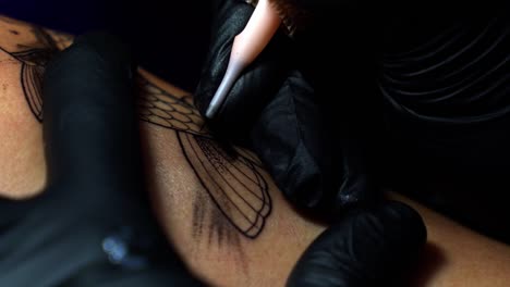 close up slow motion handheld shot of a tattoo artist tattooing a client and adding shading with the needle penetrating the skin in a dark studio room