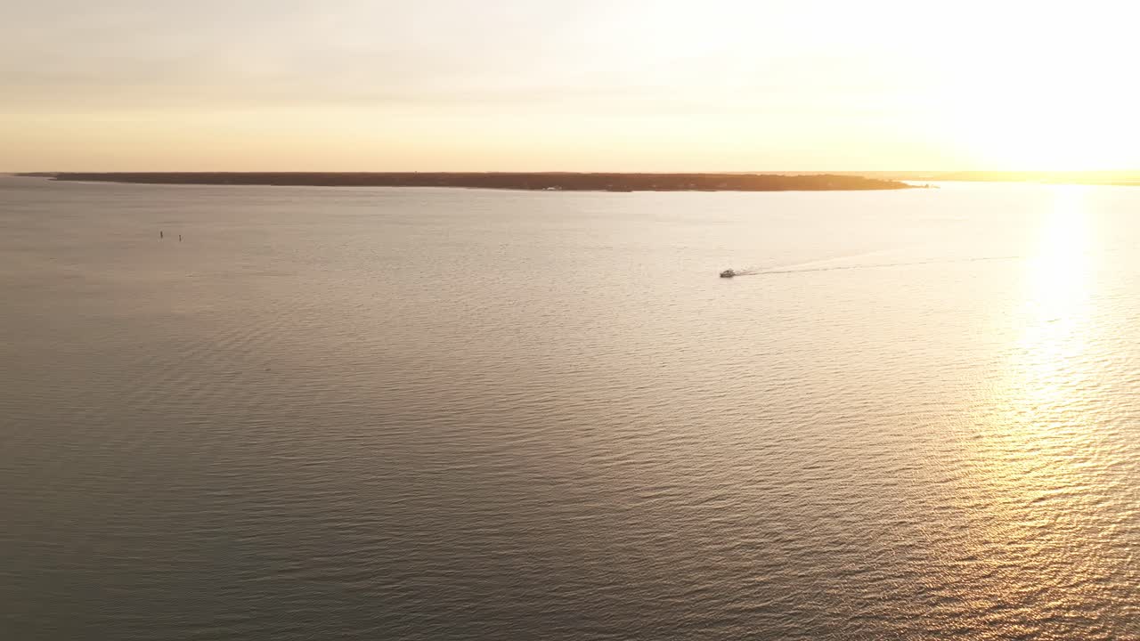 Drone pullback from single boat yacht driving leaving wake against vivid sunset sky, reflecting off the sea, Harbour Town Pier South Carolina USA