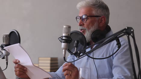 man records a podcast or interview with a microphone in a recording studio. senior sound engineer or radio host. an adult gray-haired man creates audio content