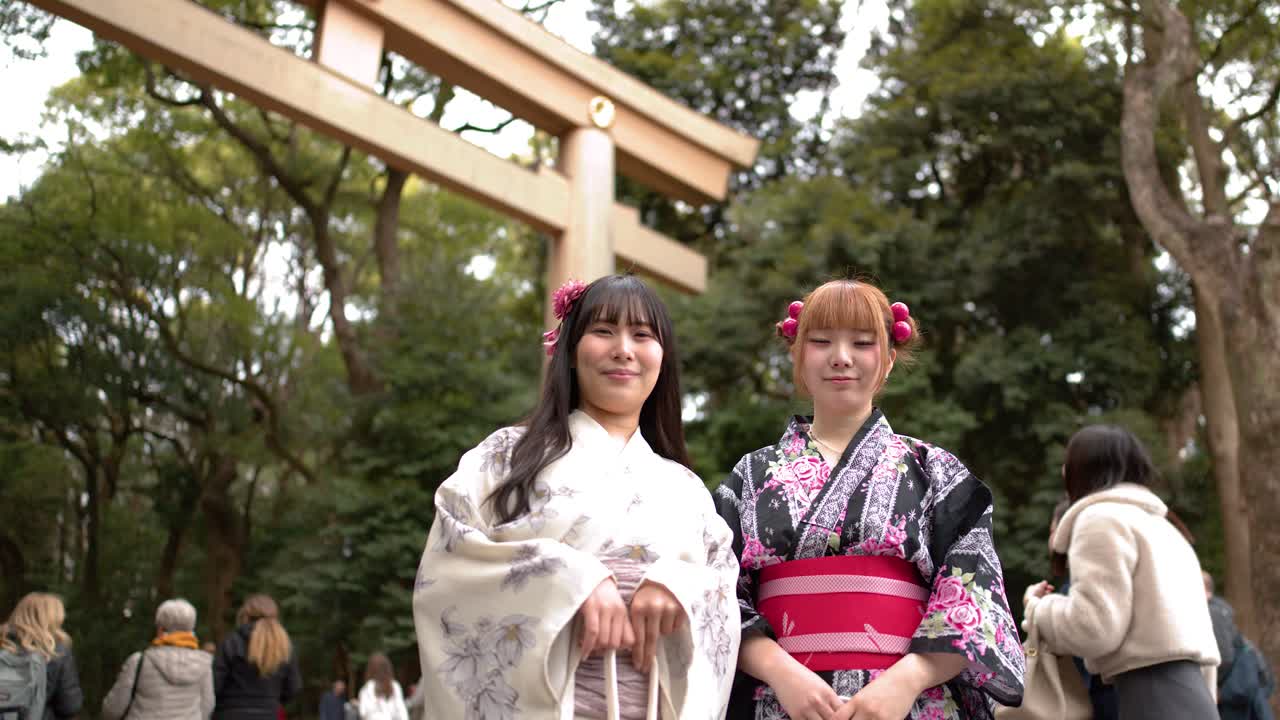 Des femmes souriantes en kimonos fleuris se tiennent devant un grand portail torii en bois à Tokyo