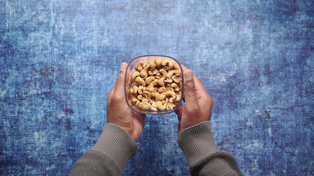 Hands Holding a Bowl of Cashew Nuts on Blue Background