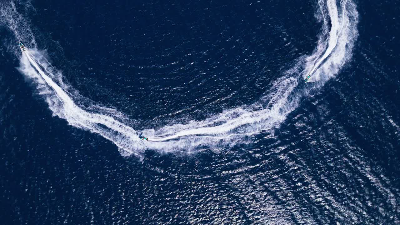 Aerial top down tracking rotates with a single jet ski creating a sharp turn, forming a curved wake in dark blue ocean waters