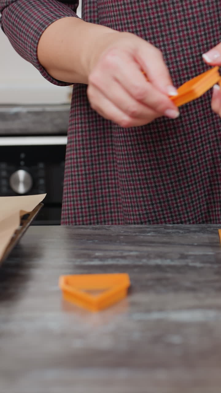 panadero en vestido a cuadros arregla formas de horneado naranja en la encimera en la cocina moderna, preparándose para hacer pasteles con iluminación cálida, backsplash de azulejos y vela roja en el fondo