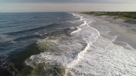 backwards drone move over waves and surf crashing on beach close up and low down