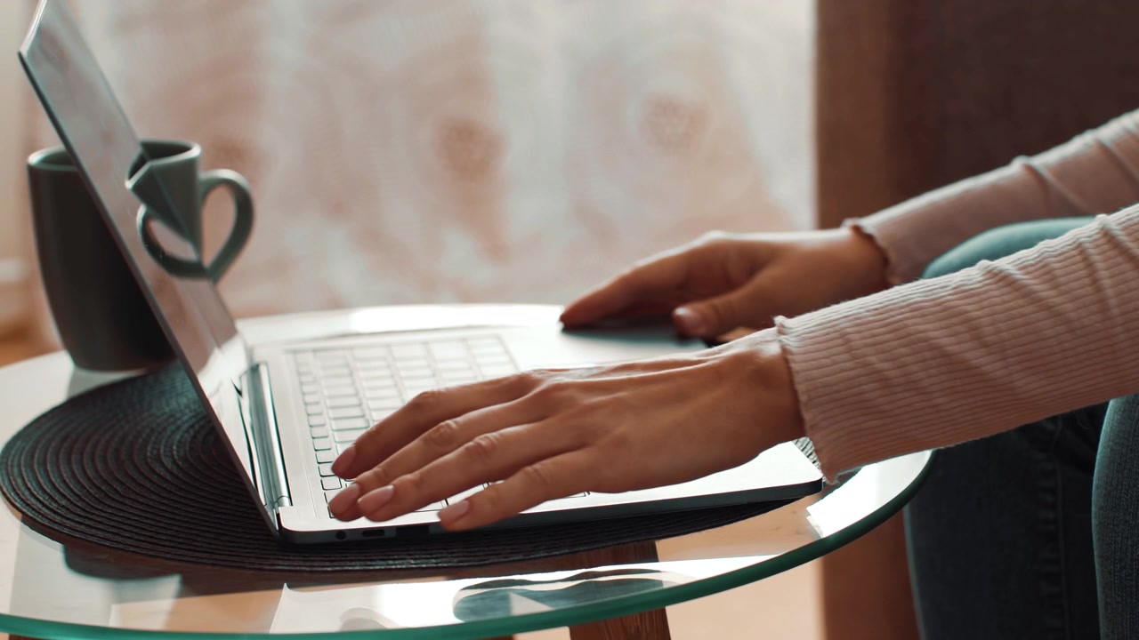 Persoon opent laptop op glazen tafel in gezellige omgeving